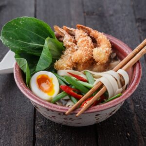 Asian spicy seafood noodle soup with tempura shrimp and greens, close view