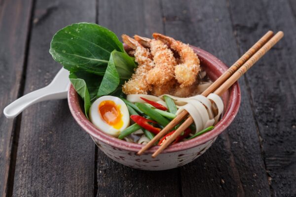 Asian spicy seafood noodle soup with tempura shrimp and greens, close view