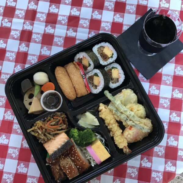 Overhead flat lay of a Japanese bento box and a glass of wine on a red and white tablecloth